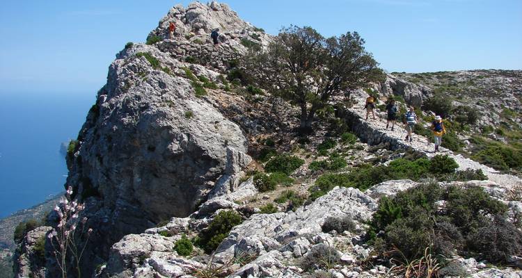 Randonneurs sur un sentier de montagne rocheux avec vue sur l'océan.