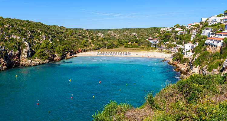 Une plage de sable dans une crique avec des parasols et un ciel bleu clair.