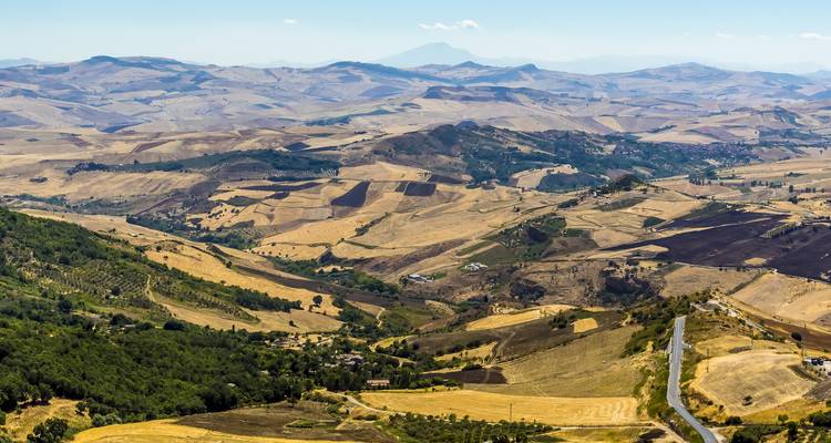 Vast landscape of rolling hills with fields and a distant mountain.