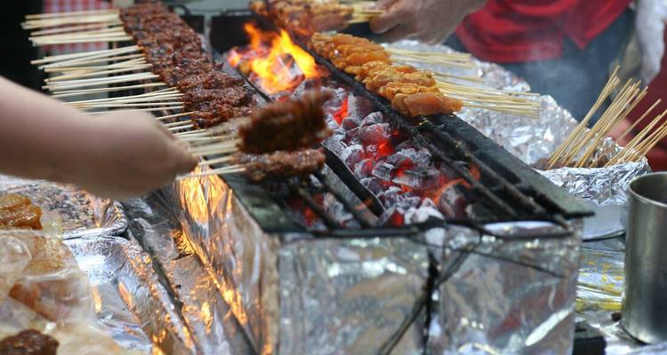 Street food vendor cooking satay skewers over an open flame.