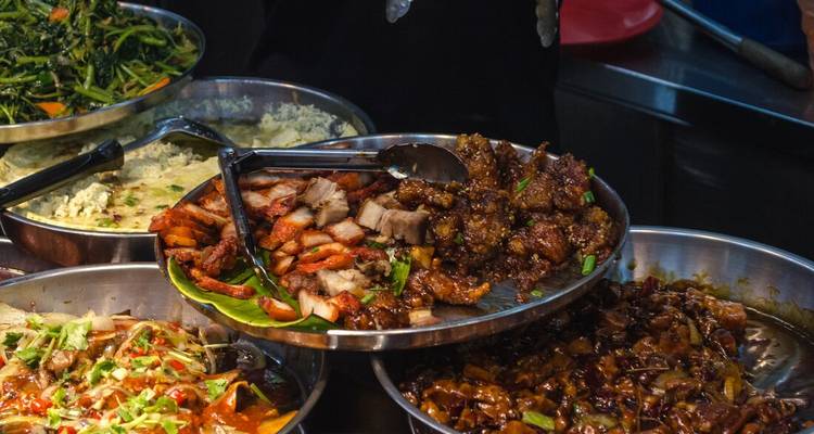 A variety of local dishes arranged on trays at a food stall.
