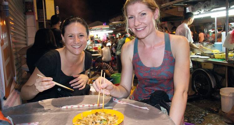 Twee vrouwen die genieten van een maaltijd op een straatmarkt.