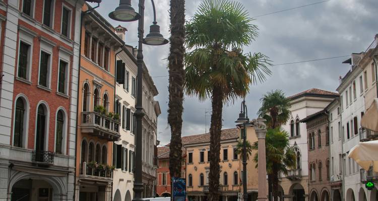 Bâtiments historiques dans une rue européenne avec des palmiers et un ciel nuageux.