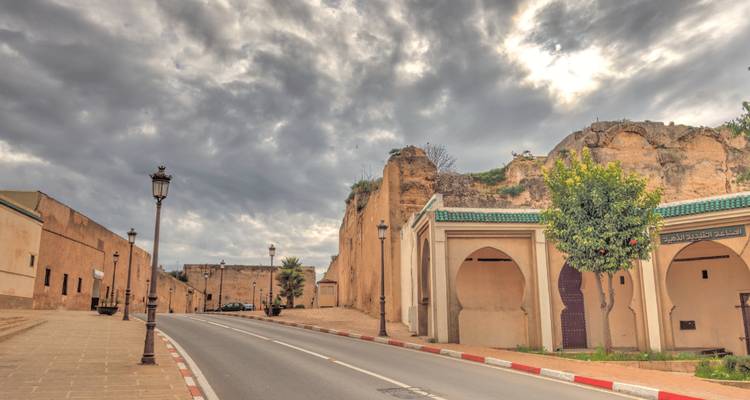 Street in Meknes with historic walls and cloudy sky.