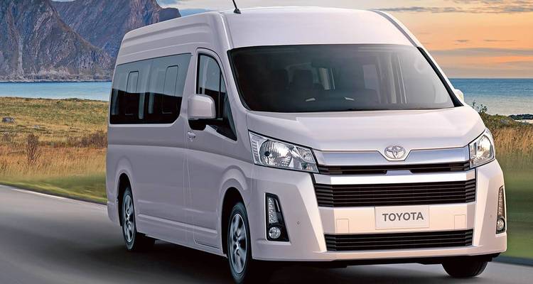 Un van Toyota blanc roulant sur une route avec un arrière-plan montagneux.