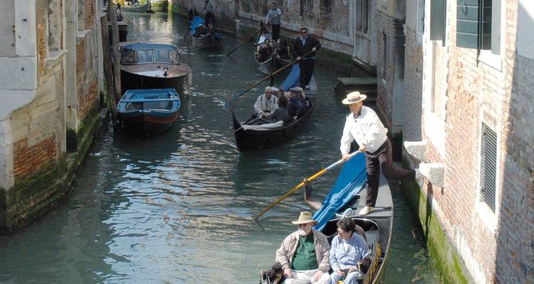 Gondoliers guiding gondolas through a narrow Venetian canal.