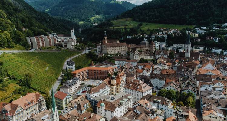 Vue aérienne d'une ville alpine avec des collines et une architecture historique.