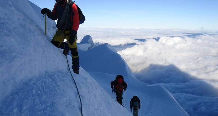 Bergbeklimmers die aan elkaar vastgesjord zijn beklimmen een besneeuwde bergkam hoog boven de wolkenlaag.