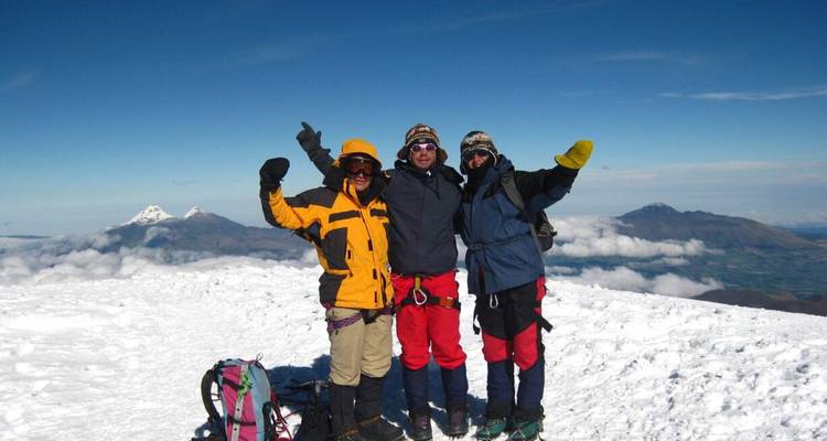 Drie klimmers vieren feest op een met sneeuw bedekte bergtop met vulkanen zichtbaar op de achtergrond.