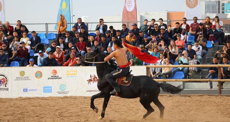 Horse rider performing with a Kyrgyz flag, with a crowd in the background.