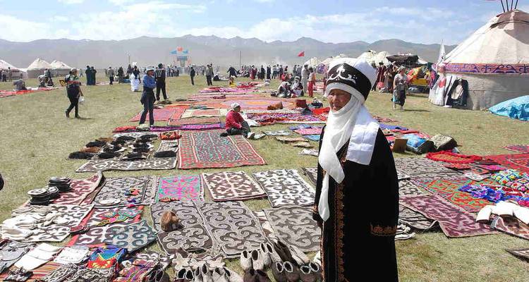 Traditional Kyrgyz market with textiles and yurts, mountains in the background.