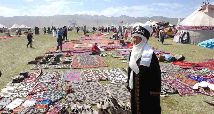 Mercado al aire libre con personas vendiendo alfombras tradicionales y artesanías en un campo.