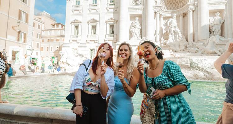 Three women enjoying ice cream in front of a grand fountain.