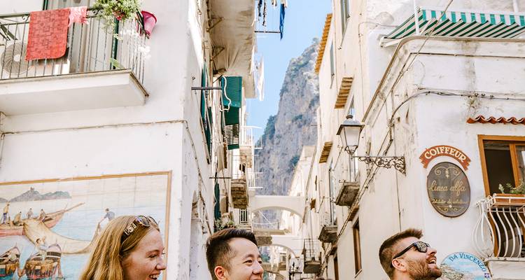 Tourists exploring a narrow Italian street with mountainous backdrop.