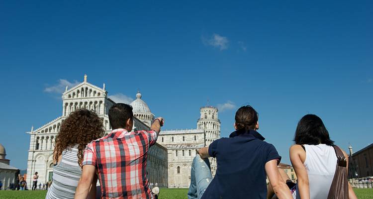 People sitting on a lawn with the Leaning Tower of Pisa in the background.