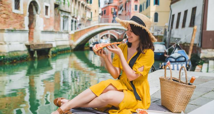 Une femme savourant une part de pizza au bord d'un canal vénitien pittoresque.
