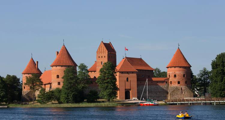 A medieval castle with red rooftops by a body of water, with people in pedal boats.