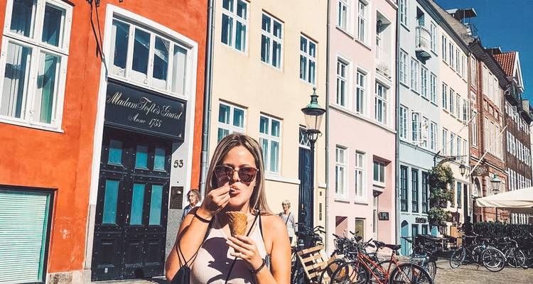 Eine junge Frau genießt ein Eis entlang Kopenhagens bunter Nyhavn-Uferpromenade an einem sonnigen Tag.