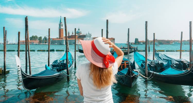 Person in red-striped hat admiring boats in Venice.
