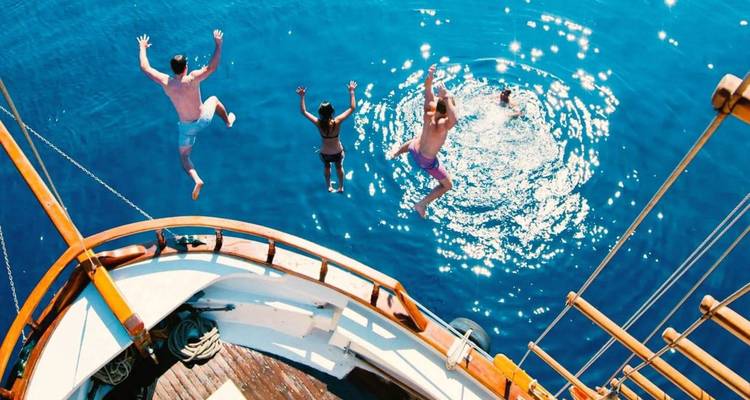 Reizigers springen van een houten zeilboot in het glinsterende Egeïsche water.