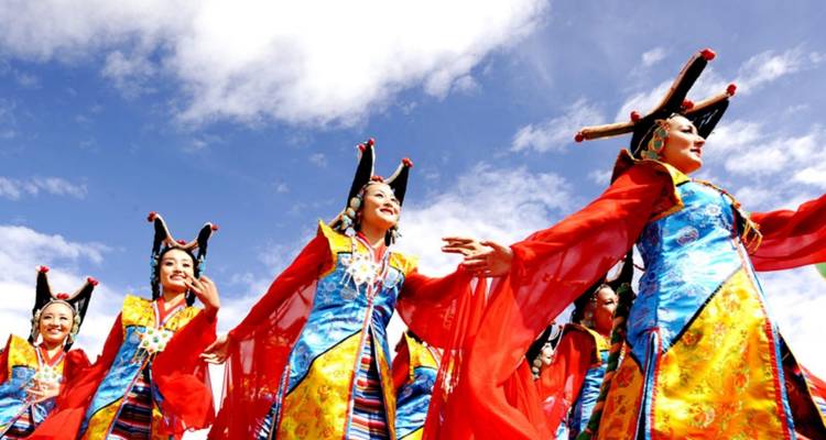 Een groep performers in levendige traditionele kostuums die dansen onder een blauwe hemel.