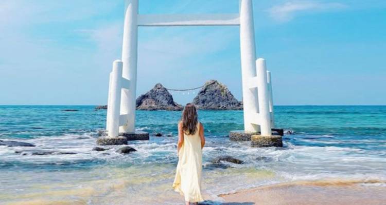 Woman standing in front of a seaside torii gate.