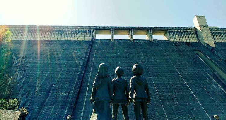 Three people facing a large dam structure.