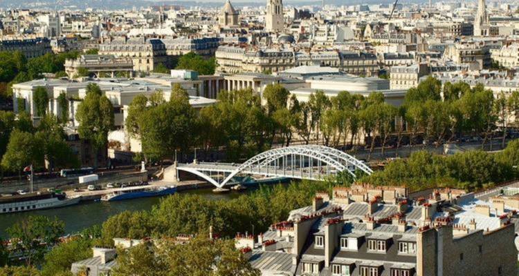 Vue d'une ville avec une rivière et un pont au milieu des arbres et des toits.