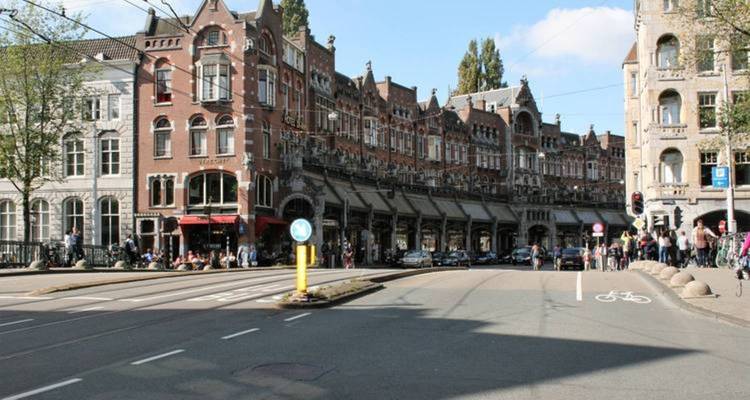 Rue urbaine avec des bâtiments historiques et des arbres bordant la rue.