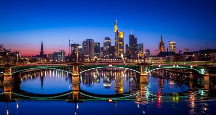 Colorful view of Frankfurt skyline during sunset with bridge reflection.
