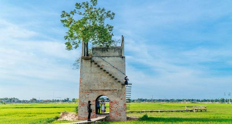 Unusual tower structure in the middle of a field with people nearby.