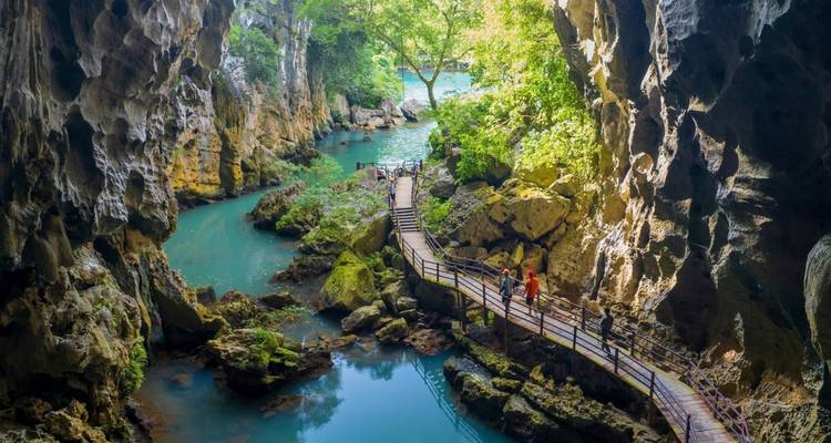 People exploring a cave with a footbridge over turquoise water.