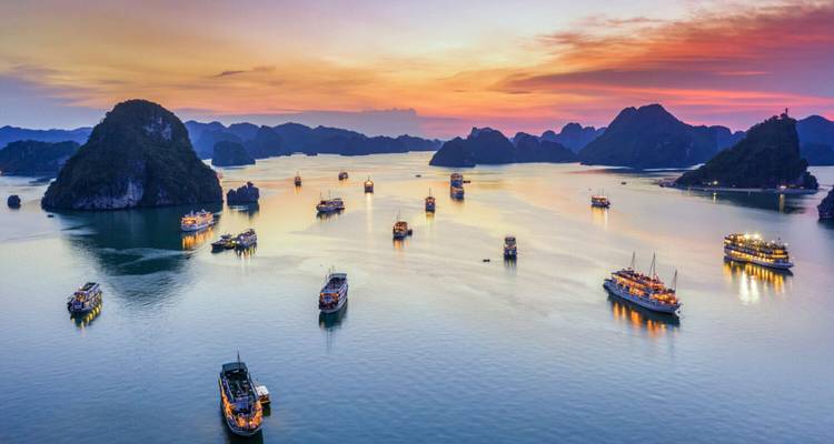 Halong Bay at sunset with boats dotting the water.
