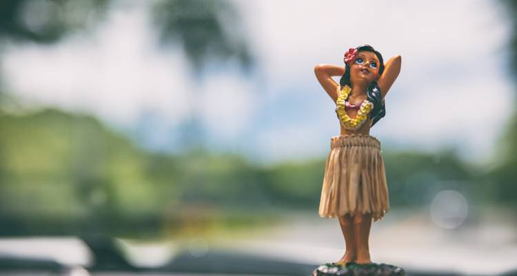 Klein hula meisje dashboard ornament met onscherpe tropische achtergrond.