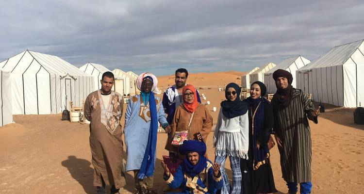 Groupe de personnes en tenue traditionnelle dans un campement du désert.