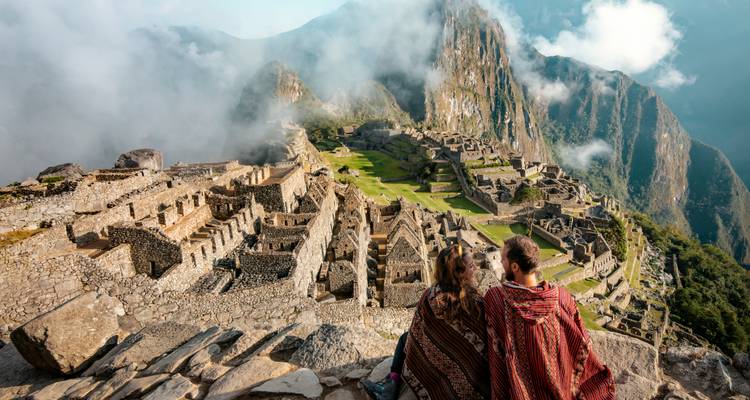 Two people wrapped in traditional blankets, overlooking Machu Picchu.