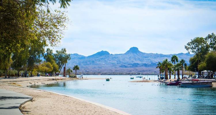 Lakeside beach with leisure boats and mountain views.