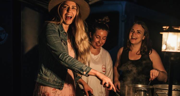 Three women enjoying a cooking activity in an outdoor setting at night.