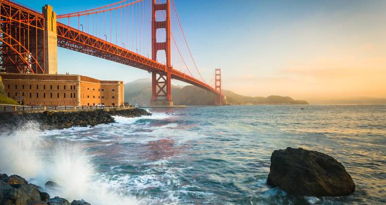 Ocean waves crashing against the rocks under the Golden Gate Bridge.