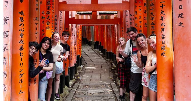 Groupe de touristes posant dans un tunnel de torii orange éclatants.