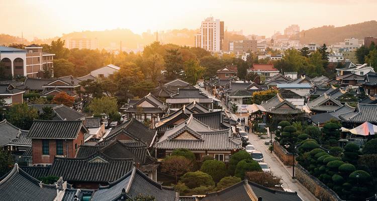 Aerial view of Jeonju Hanok Village with traditional roofs and modern city background.