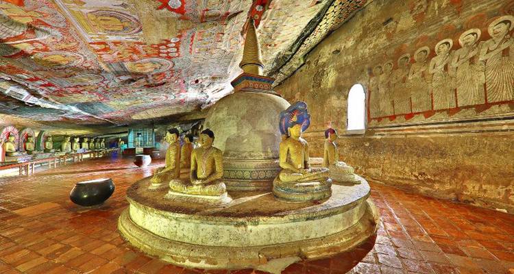 Salle de temple rupestre peinte de manière complexe avec des statues de Bouddha autour d'un stupa central sur un sol carrelé.