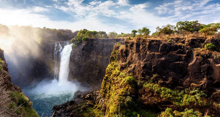 Die donnernden Victoriafälle stürzen in eine nebelverhangene Schlucht, umgeben von üppiger Klippenvegetation.