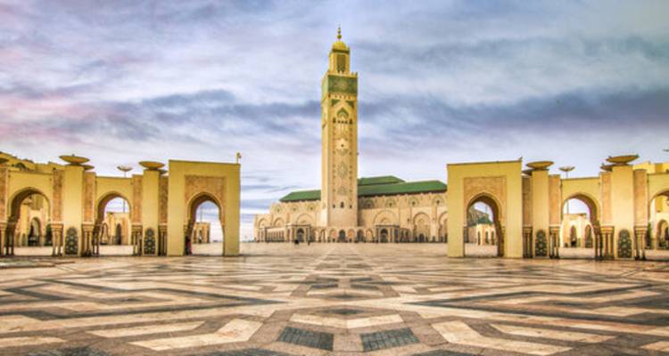 De grootse Hassan II-moskee torent uit boven het geometrische plein onder de pastelkleurige dageraadhemel in Casablanca.