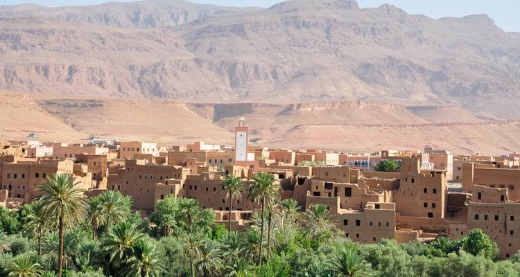 Leemstenen dorp en palmenoase strekken zich uit onder droge Atlasvoorheuvels in warm woestijnlicht.