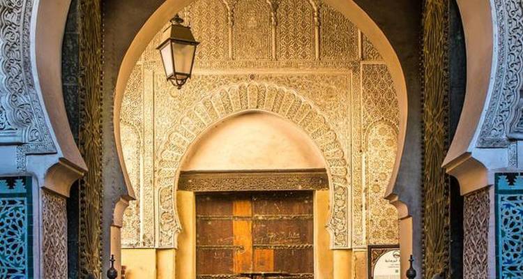 Ingewikkeld uitgesneden Moorse booggang met sierlijke houten deur en hangende lantaarn in Marokkaanse medina.
