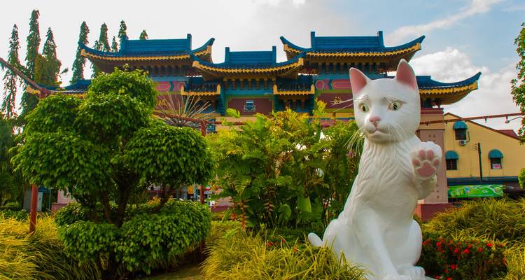 Groot wit kattenbeeld dat met een poot zwaait voor een kleurrijke Chinese poort in Kuching.