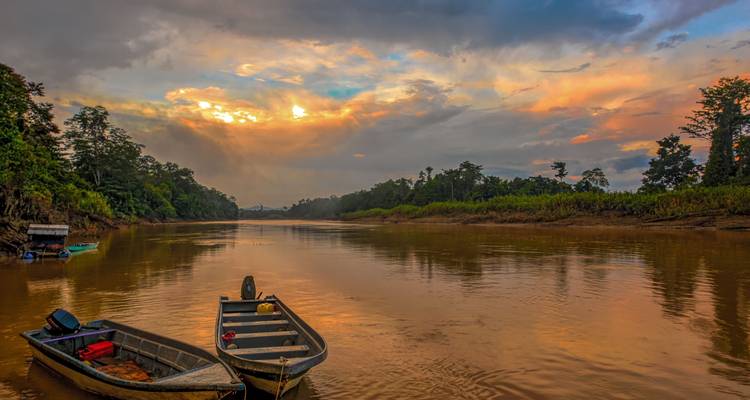Twee kleine boten op de gouden Kinabatangan-rivier bij zonsondergang met een dramatische door wolken verlichte hemel.