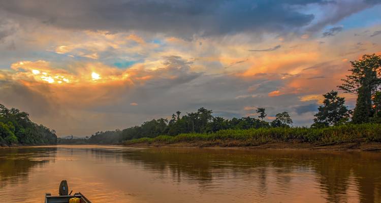 Wijd uitzicht op de Kinabatangan-rivier die dramatische, kleurrijke avondwolken weerkaatst.