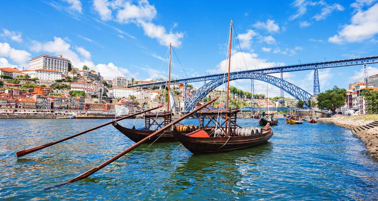 Traditionelle Rabelo-Boote vertäut am Douro mit Portos buntem Hügelhang und der Dom Luís I Brücke im Hintergrund